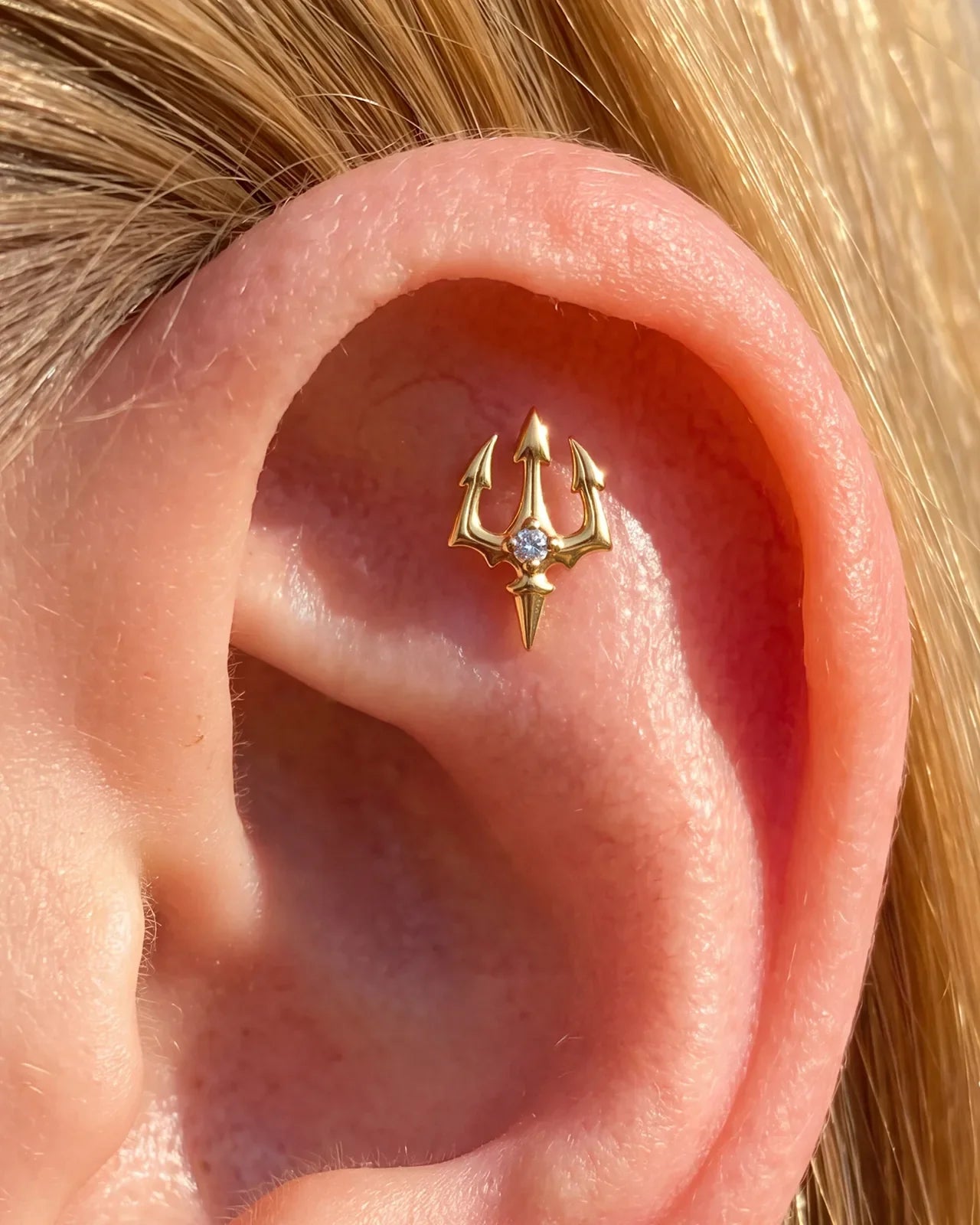 Gold Abyssal Trident flatback stud worn in an ear piercing