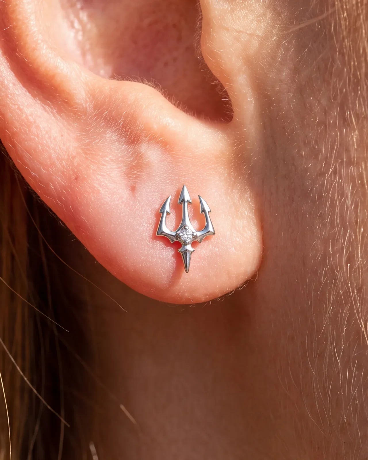 Silver Abyssal Trident flatback stud worn in an ear piercing